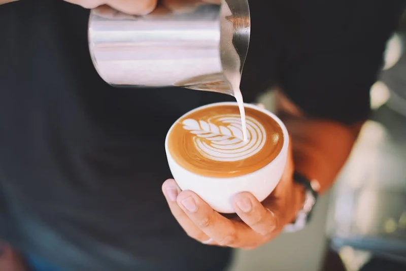 Barista versant du lait pour créer du latte art, montrant un motif de cœur