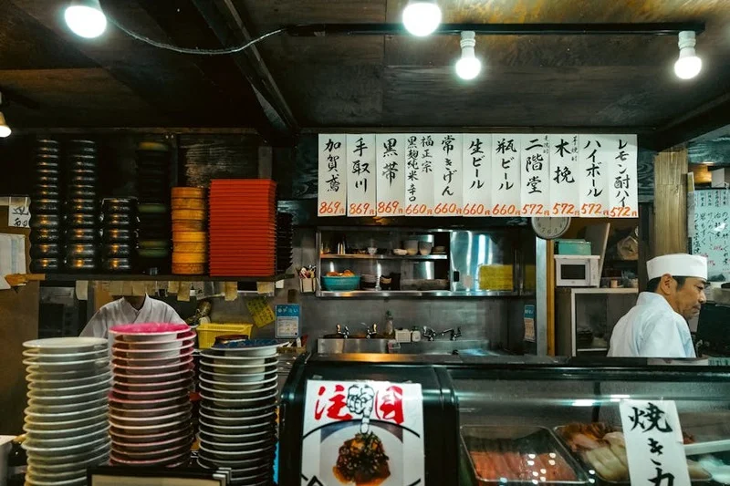 Vue aérienne d'un bar à sushis animé avec un long comptoir, montrant diverses assiettes de sushis et des chefs au travail