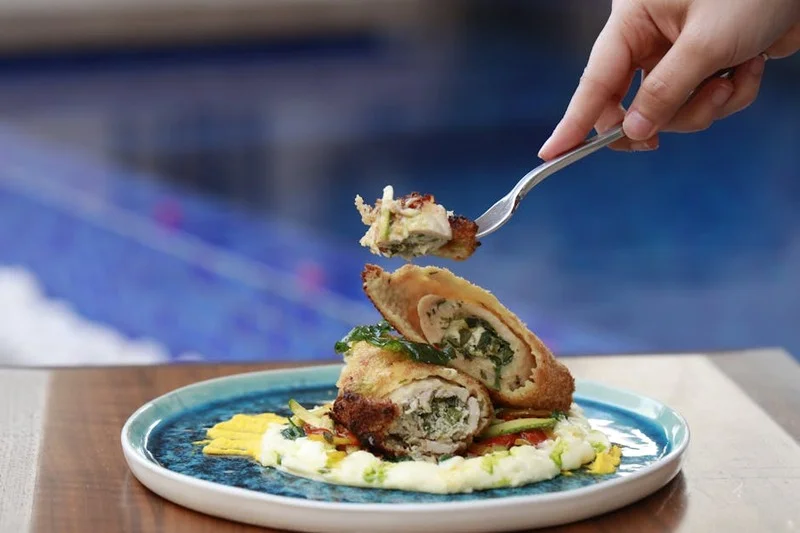 Une main tenant une fourchette, prête à déguster un plat magnifiquement présenté, avec un arrière-plan de restaurant flou