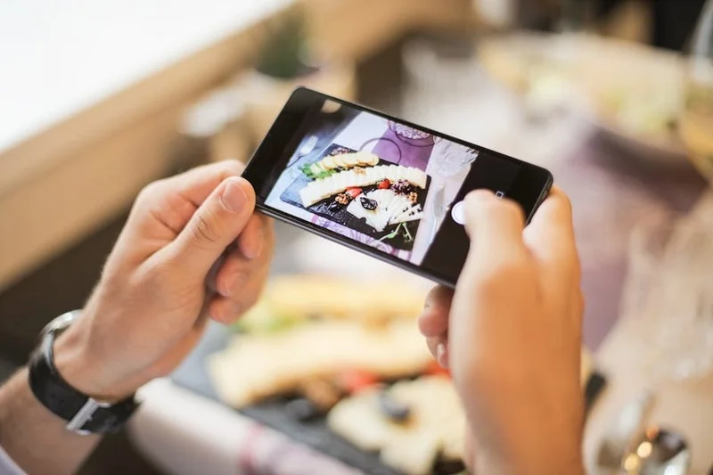 Une personne tenant un smartphone et photographiant un plat gastronomique magnifiquement présenté