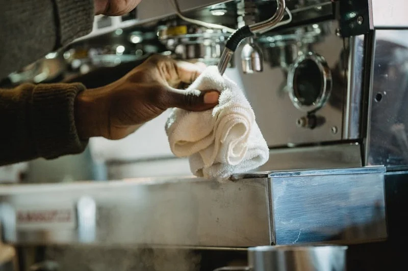 Une personne nettoyant une machine à expresso avec une brosse et une solution de nettoyage